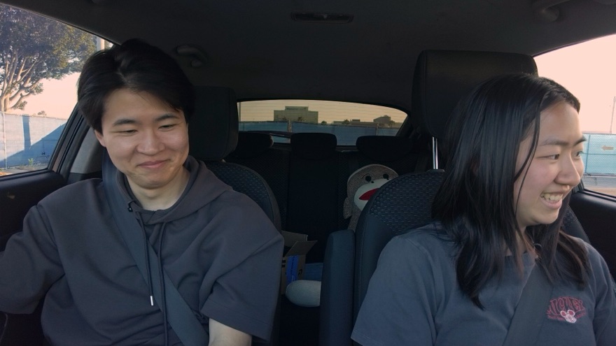 Yuji and a student smiling in the car, parked in an empty lot